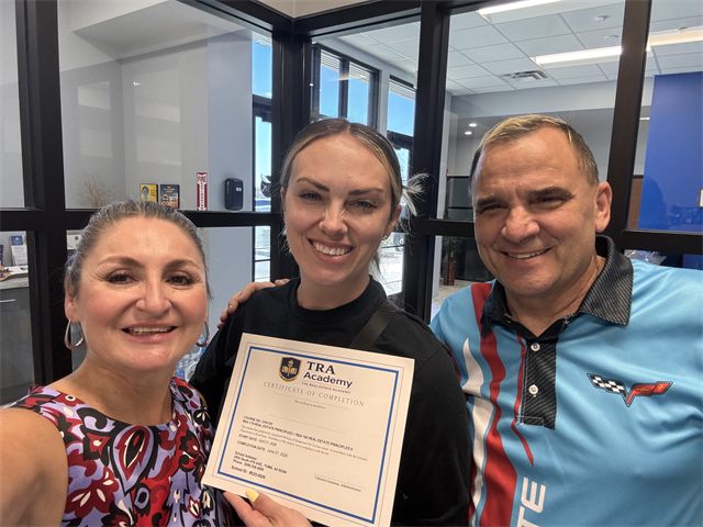 A TRA Academy student holding their certificate of completion with instructors Nora Acosta and John Endres